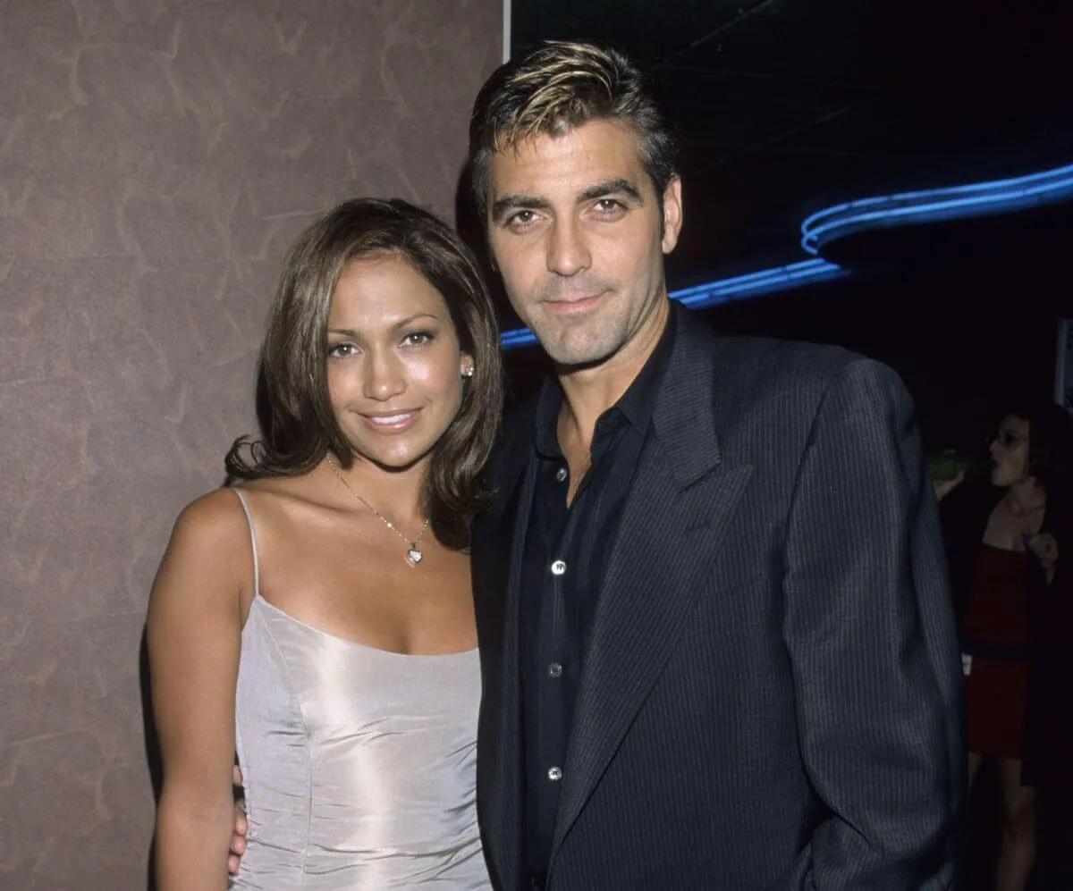 Jennifer Lopez wears a silver dress and stands with George Clooney, who wears a black suit.